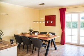 A dining area with a table, chairs, a vase with flowers, and a red curtain.