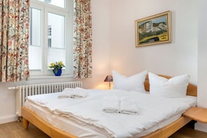 Ein Hotelzimmer mit Bett, weißer Bettwäsche, einem Gemälde an der Wand und einem Fenster mit Vorhängen.