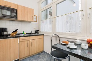 A kitchen with wooden cabinets, a microwave, a coffee maker, and a dining area with a table set for breakfast. - Marie-Luise at Villa Stranddistel (Ostseebad Binz)