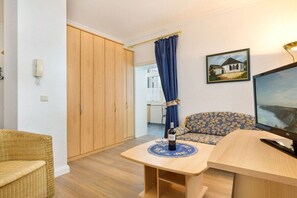 Ein Zimmer mit einem Holzschrank, einem blumengemusterten Sofa, einem kleinen Tisch mit einer Weinflasche und einem Fernseher auf einem Holzgestell.