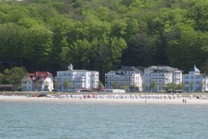 Un hôtel situé sur la côte, composé de plusieurs bâtiments, avec une plage et une colline boisée.