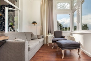 A room with a grey sofa, a small table, a chair, and a window with a view of buildings. - Beach jewel - Villa Agnes (Binz)