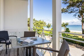 A balcony with a table and chairs, overlooking a beach and trees. - No. 5 (Summer Wind) in Villa Helene (Ostseebad Binz)