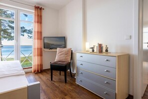 A room with a bed, a chair, a television, a dresser, and a view of the sea through a window. - No. 5 (Summer Wind) in Villa Helene (Ostseebad Binz)