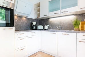 Una cocina moderna con armarios blancos, encimera de mármol, cafetera y pileta.
