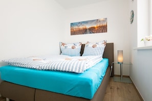 A bedroom with a bed, a nightstand with a lamp, a wall-mounted picture, and a window with a view. - Holiday apartment with 2 bedrooms (Zinnowitz)