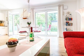 A modern living room with a red sofa, a dining area with a table set for two, and a bookshelf filled with books. - Holiday apartment with 2 bedrooms (Zinnowitz)