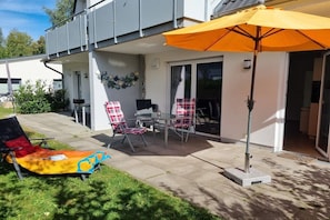 An outdoor patio area with a table and chairs, a sun lounger, and a large umbrella. - Holiday apartment with 2 bedrooms (Zinnowitz)
