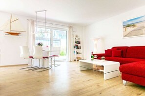 A modern living room with a red sofa, a white coffee table, and a dining area with white chairs. - Holiday apartment with 2 bedrooms (Zinnowitz)