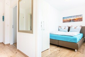 Un dormitorio con cama, un espejo grande, un cuadro en la pared y suelo de madera.