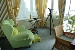 A room with a green armchair, a wicker chair, a telescope on a tripod, and a small table with books and a candle. - (No. 8) in Villa Fortuna (Bansin)