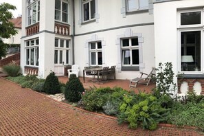 A two-story building with a patio area featuring outdoor furniture, a brick pathway, and various plants. - Holiday apartment with 1 bedroom (Zinnowitz, Usedom, Usedom-Nord)
