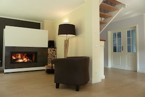 Ein Wohnzimmer mit Kamin, Lampe, Sessel und Treppe.