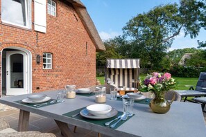 A dining table set outdoors with a brick house in the background. - Lokelk Hüs (Happy House) (Süderende \/ Föhr)