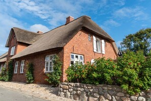 A brick house with a thatched roof, white windows, and a stone wall in front. - Lokelk Hüs (Happy House) (Süderende \/ Föhr)