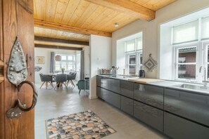 A modern kitchen with dark cabinets, a large window, and a dining area with a table and chairs. - Lokelk Hüs (Happy House) (Süderende \/ Föhr)