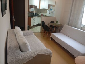 Ein kompakter Wohnbereich mit einer Couch, einem kleinen Esstisch mit Stühlen und einer Küchenzeile im Hintergrund.