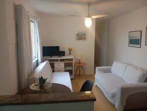 Een kamer met een bed, een bureau met een computer, een stoel, een klein tafeltje met een lamp en een plafondventilator.