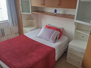 A hotel room with a bed, a red blanket, a white pillow, and a small blue vase on a shelf. - Very quiet and safe apartment near Barra, 24-hour doorman, shops. (Rio de Janeiro)