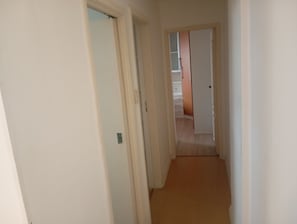A narrow hallway with carpeted flooring leading to a room with a bed and a dresser. - Very quiet and safe apartment near Barra, 24-hour doorman, shops. (Rio de Janeiro)