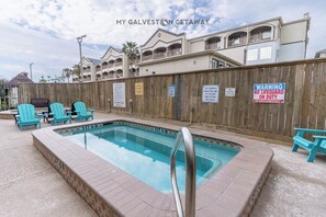 A pool area with a wooden fence, a sign indicating no lifeguard on duty, and a sign warning about hot tubs. - Wade 'N Sea Condo with Pools & Hot Tubs (Galveston)