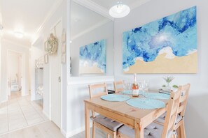 A dining area with a wooden table, chairs, and a large abstract painting on the wall. - Wade 'N Sea Condo with Pools & Hot Tubs (Galveston)