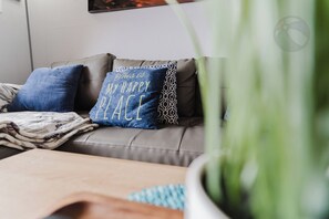 A living room with a grey sofa, a blue pillow with text, and a green plant in the foreground. - Wade 'N Sea Condo with Pools & Hot Tubs (Galveston)