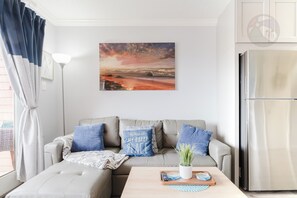 A living room with a sofa, a coffee table, a painting, and a refrigerator. - Wade 'N Sea Condo with Pools & Hot Tubs (Galveston)