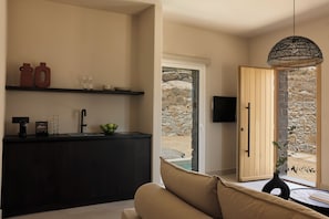 A modern kitchen with a black countertop, a sink, and a window overlooking a stone wall. - Naxian Rhapsody Luxury Villas & Suites (Naxos)