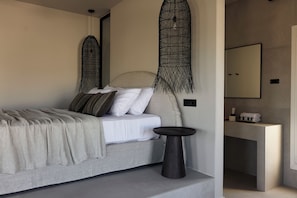 A modern bedroom with a bed, bedside table, and a bathroom with a counter and mirror. - Naxian Rhapsody Luxury Villas & Suites (Naxos)