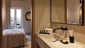 A hotel room with a bed, a bathroom with a sink, and a large mirror. - Naxian Rhapsody Luxury Villas & Suites (Naxos)
