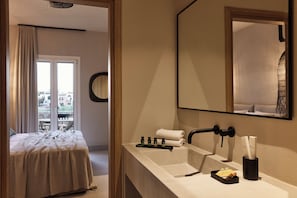 A hotel room with a bed, a bathroom with a sink, and a large mirror. - Naxian Rhapsody Luxury Villas & Suites (Naxos)