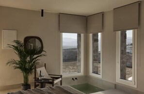 A room with a large window, a bathtub, a potted plant, and a mirror. - Naxian Rhapsody Luxury Villas & Suites (Naxos)