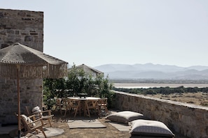 An outdoor seating area with a stone wall, wooden furniture, and a view of mountains and a body of water. - Naxian Rhapsody Luxury Villas & Suites (Naxos)