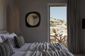 Un dormitorio con cama, almohadas, una colcha, una lámpara colgante, un espejo y vistas al exterior.