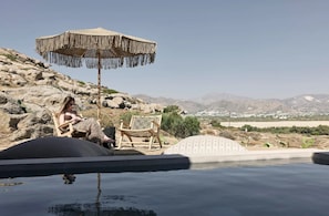 A pool area with a lounge chair and a woven umbrella. - Naxian Rhapsody Luxury Villas & Suites (Naxos)