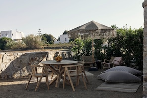 A round wooden table with chairs, a woven umbrella, and a stone wall in the background. - Naxian Rhapsody Luxury Villas & Suites (Naxos)