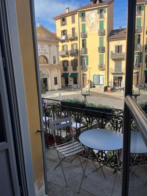 A balcony with outdoor seating, overlooking a street with buildings and a church. - San Rocco Apartment in Verbania (Verbania)