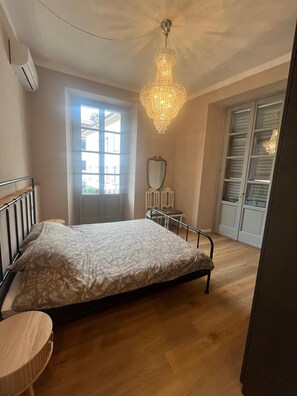 A bedroom with a bed, a chandelier, a window, and a wardrobe. - San Rocco Apartment in Verbania (Verbania)