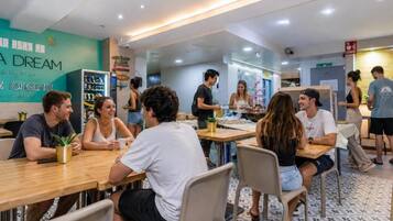 Un espacio de comedor informal con mesas y sillas, un refrigerador, y una pared con texto y una planta.