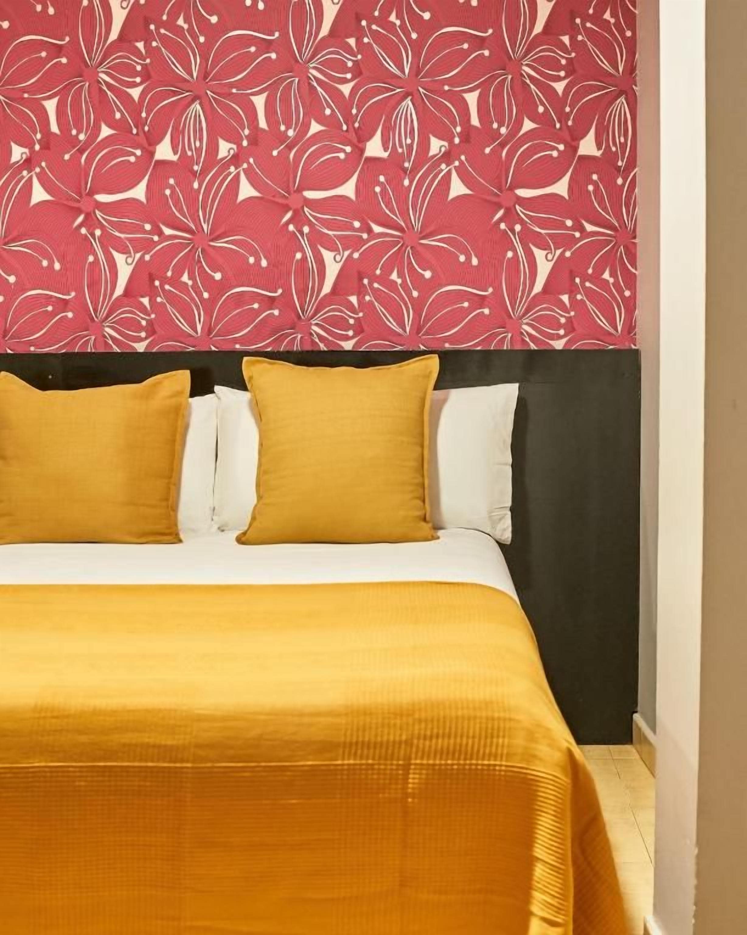 Een bed met een geel sprei en twee kussens, een zwart hoofdbord en een muur met een bloemenmotief.