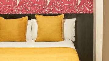 Een bed met een geel sprei en twee kussens, een zwart hoofdbord en een muur met een bloemenmotief.
