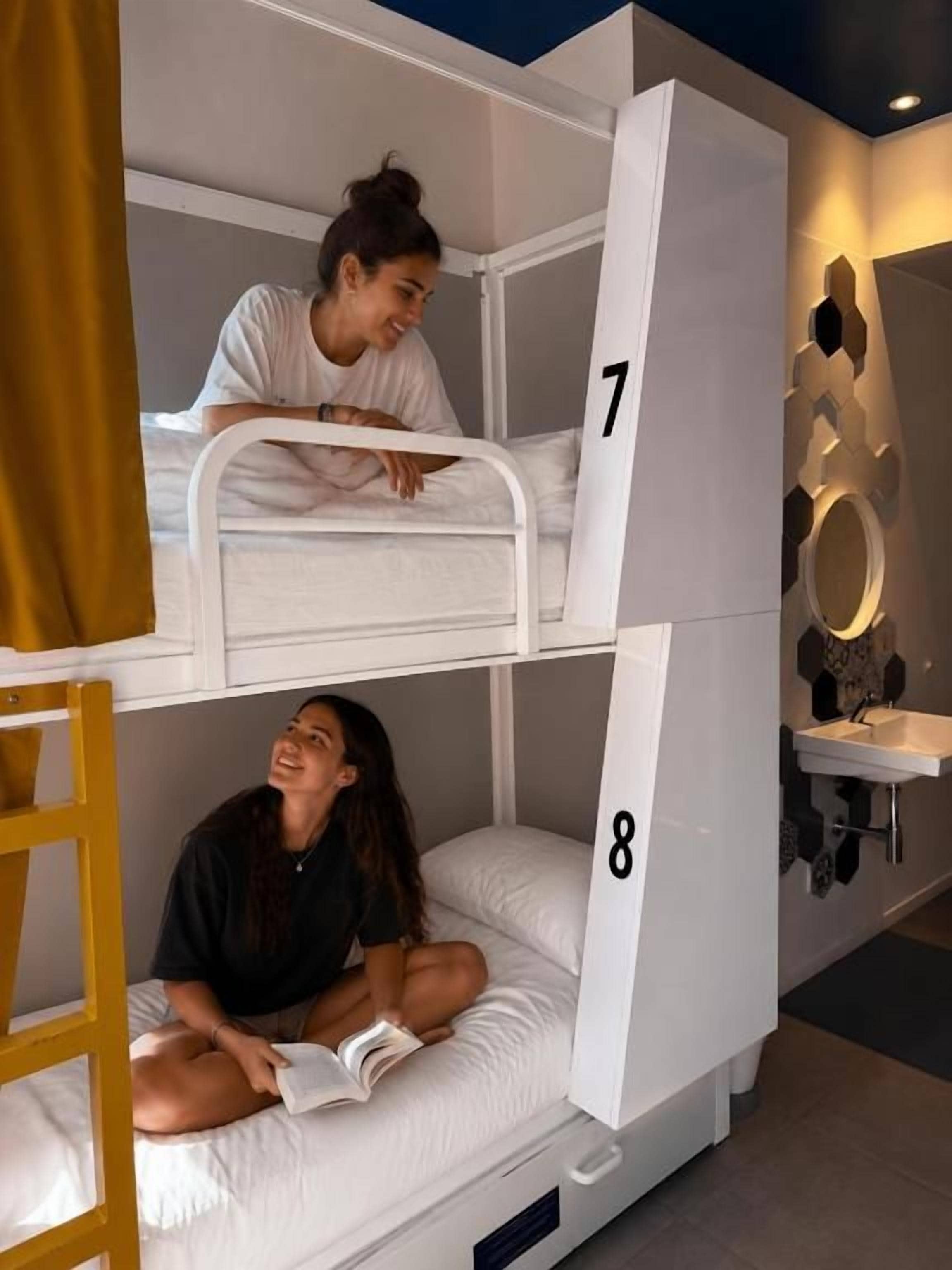 A bunk bed with two levels, each with a number. There is a ladder on the left and a sink with a mirror on the right.