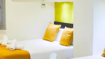 Habitación de hotel con dos camas, cada una con cubrecama amarillo y almohadas blancas, y un aire acondicionado de pared.