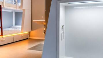 Una cama litera con una escalera, una puerta con manija y una tira de luces a lo largo de la pared.