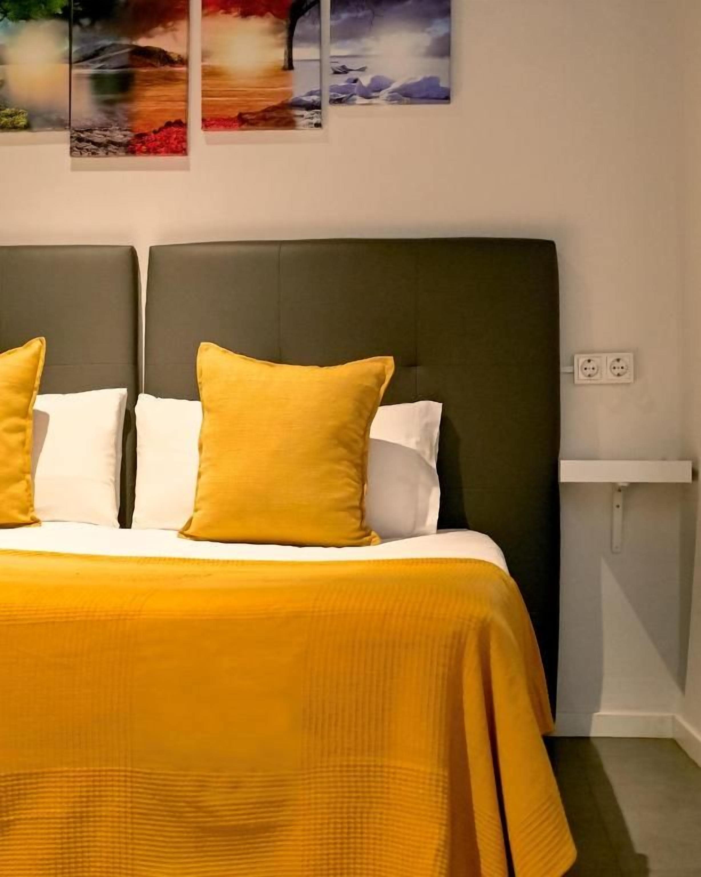 Una cama con cabecera oscura, dos almohadas y una colcha amarilla.