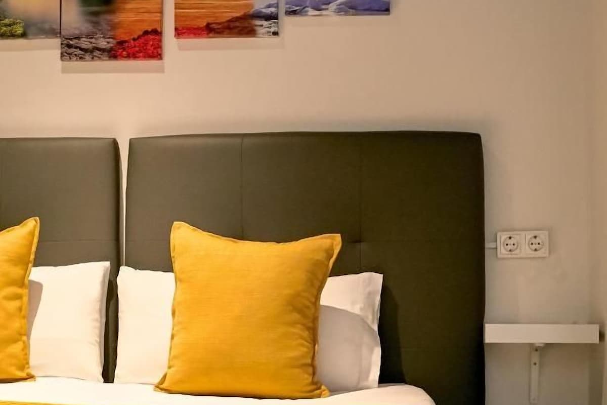 Een bed met een donker hoofdbord, twee kussens en een gele sprei.