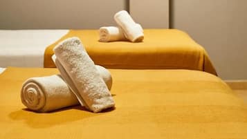 Una habitación con dos camas, cada una cubierta con una colcha amarilla y toallas blancas.