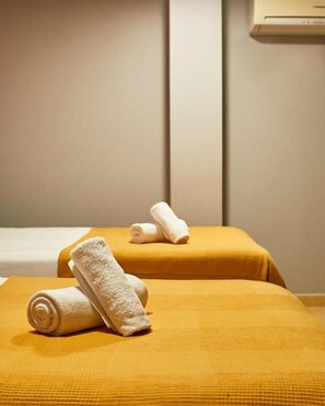 Ein Zimmer mit zwei Betten, beide mit gelber Bettdecke und weißen Handtüchern bezogen.