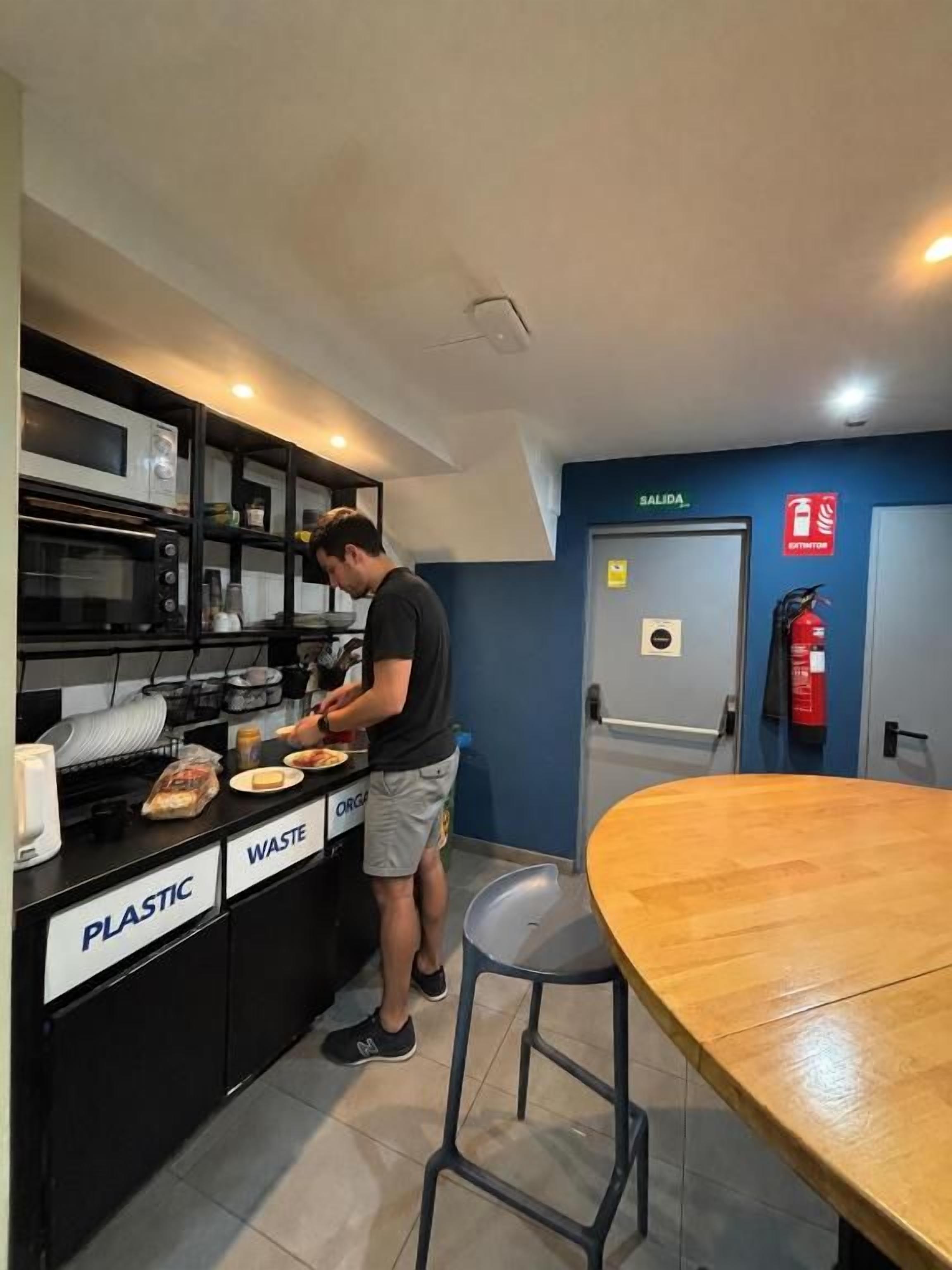 Un área de cocina con una persona preparando comida, un cubo de basura y un extintor.